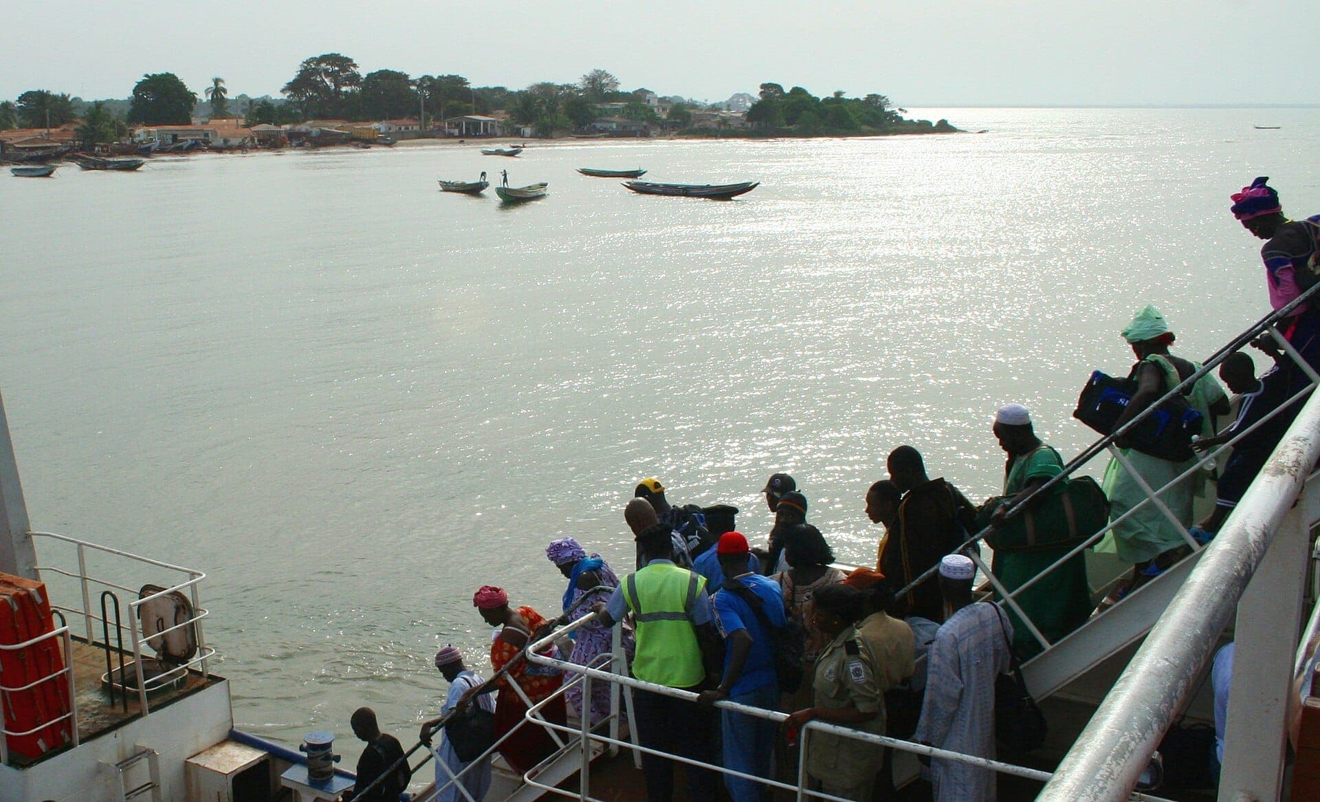 Passagers descendant du bac de Barra sur le fleuve Gambie, pirogues au mouillage devant la rive